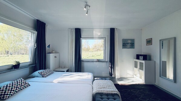 A hotel room with a bed, a desk, a window with a view of trees, a cabinet, and a mirror.