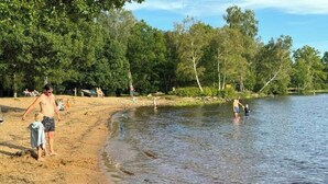 En sandstrand med folk som befinner sig nära vattnet, omgiven av träd.