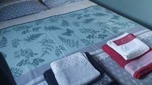 Een slaapkamer met een bed, kussens, een bedlampje en een wandplank met decoratieve objecten.