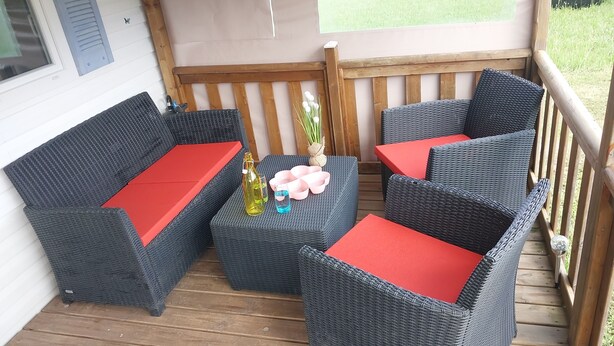 Een overdekt terras met rieten meubels en rode kussens.