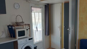 Een kleine keuken met een magnetron, wasmachine en een tafeltje met een tafelkleed met patroon.