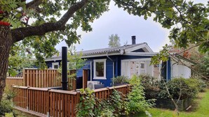 Une maison bleue avec une fenêtre blanche, entourée d’une clôture en bois et de verdure.