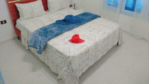 A bed with a red headboard, white patterned bedding, and a blue blanket. - VILAA TEJ EL MOULK (Somâa)