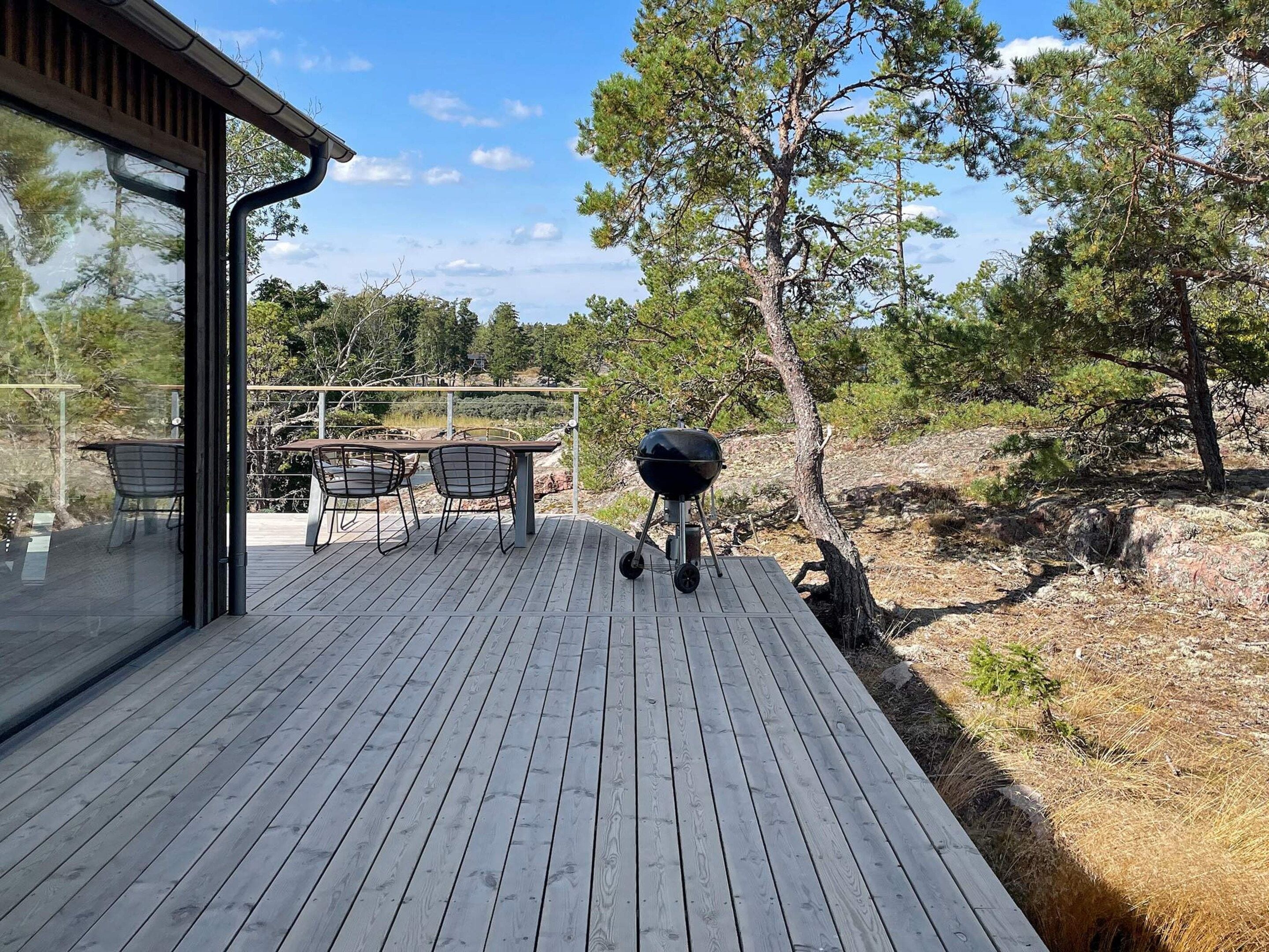 A wooden deck with a grill and chairs, overlooking a natural landscape.