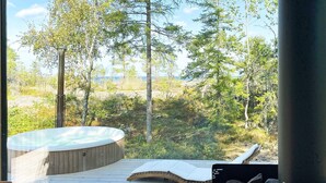 Ein Whirlpool auf einer Holzterrasse mit Blick auf einen Wald und ein Gewässer.