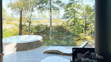 Un jacuzzi en una terraza de madera con vista a un bosque y una masa de agua.