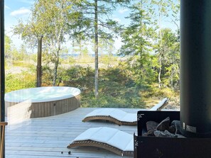 Un bain à remous sur une terrasse en bois, avec vue sur une forêt et un plan d’eau.
