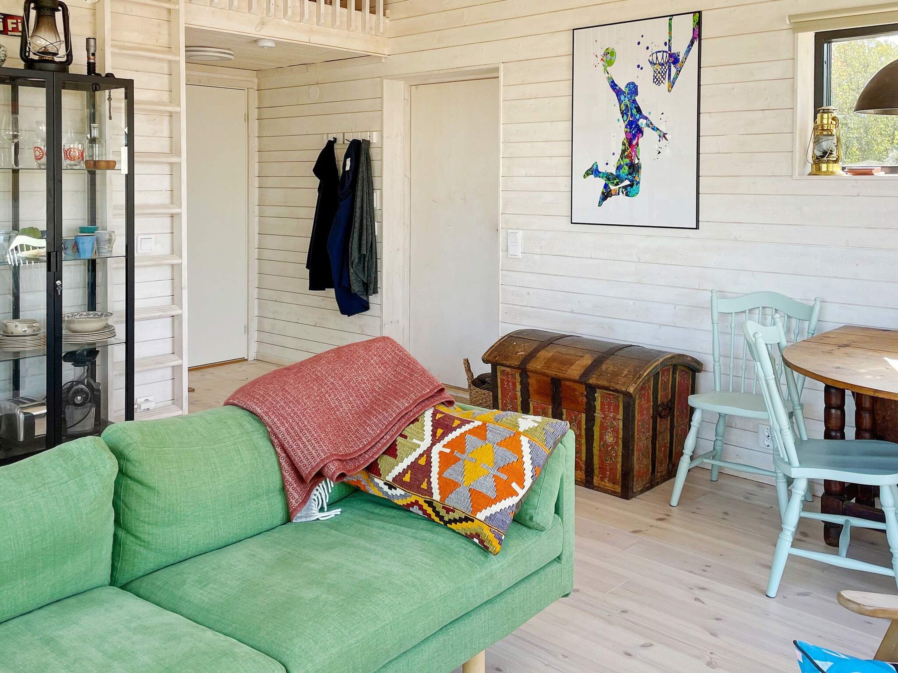 A cozy room with a green sofa, a wooden chest, a dining table with chairs, and a wall-mounted basketball artwork.