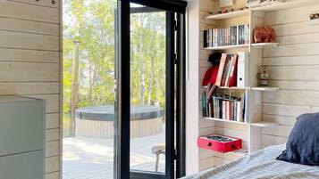 A bedroom with a large sliding glass door leading to an outdoor deck, a bookshelf filled with books, and a bed with a blue pillow.