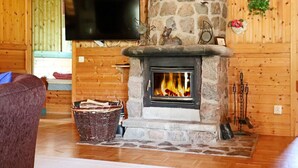 A cozy cabin interior with a stone fireplace, a television mounted on a wooden wall, and a wicker basket on the floor. - 4 Star Holiday Home in Oskarstrom (Oskarstrom)