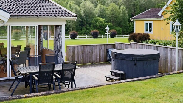 A covered outdoor patio with a table and chairs, a hot tub, and a wooden deck. - 4 Star Holiday Home in Oskarstrom (Oskarstrom)
