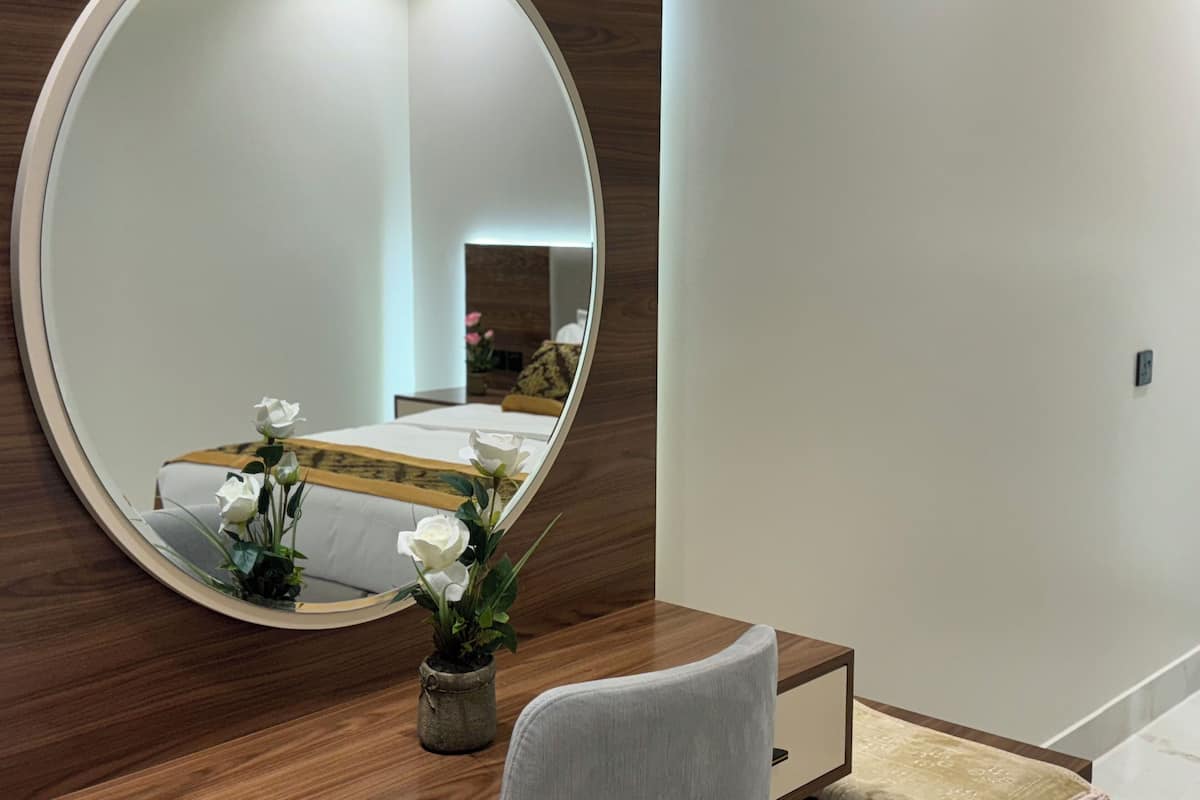 A modern bedroom with a large round mirror, a bed with a white and yellow bedspread, and a small potted plant with white flowers.