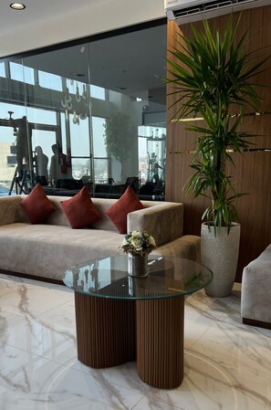 A modern living room with a glass coffee table, a sofa with red cushions, and a large potted plant. - Heaven inn 1 (Abha)