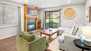 A living room with a fireplace, a television, and a view of the outdoors through a sliding glass door. - Red Pine N3 | Fireplace | Full Kitchen | Washer & Dryer | Patio | Pools & Hot Tub | Walk to Lifts (Park City)