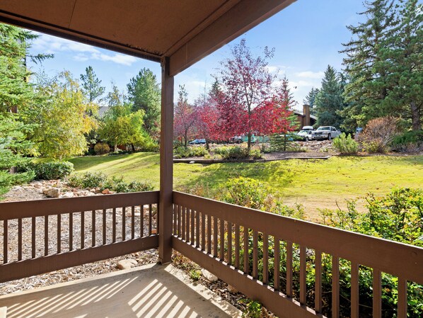 A covered porch with a view of a landscaped garden, a lawn, and a parking area with vehicles.