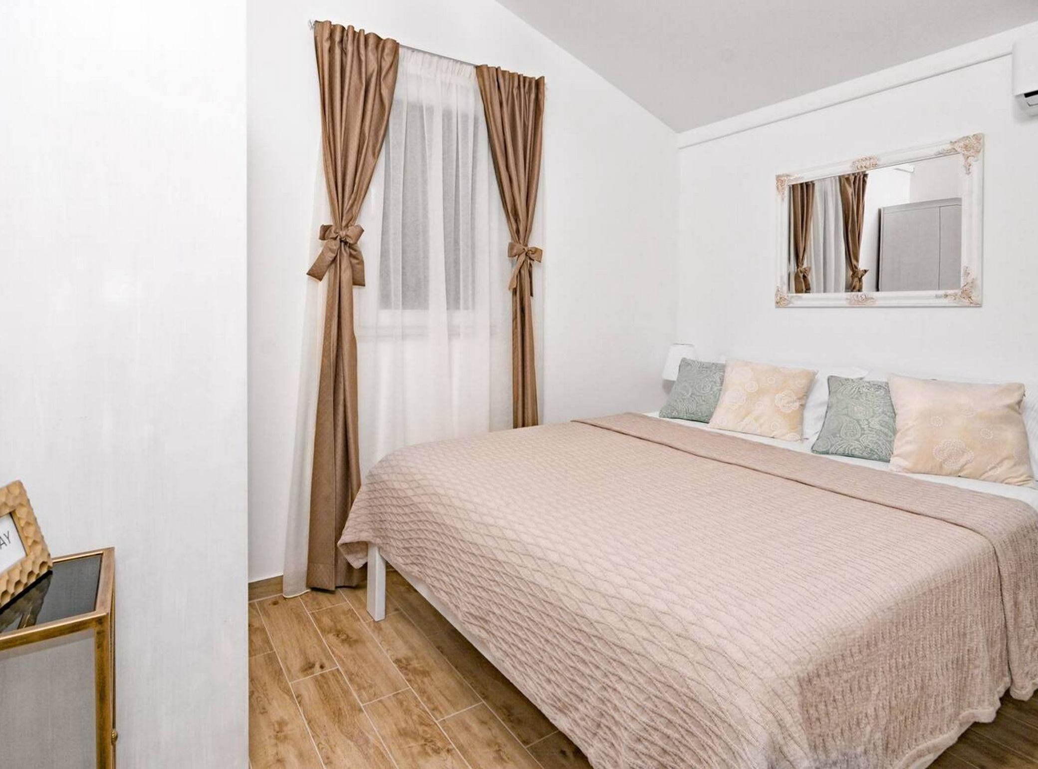 A bedroom with a bed, curtains, a mirror, and a bedside table.