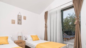 A bedroom with two beds, a bedside table, a lamp, and a view of an outdoor area with a pool and lounge chairs. - Hidden Gem Holiday Home With Pool in Kastel Stafilic (Kastela)