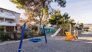 A playground with swings and slides, surrounded by trees and buildings. - Mastrinka Bright Apartment With Free Parking and Modern Amenities (Trogir)