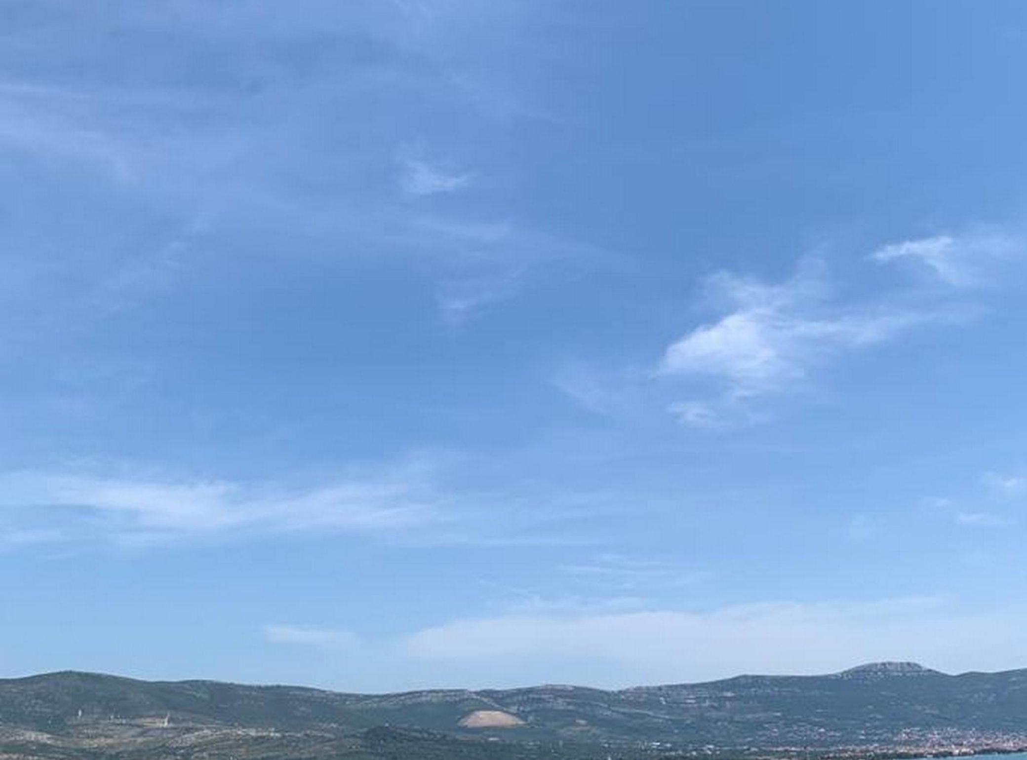 A panoramic view of a coastal landscape with rolling hills and a clear blue sky.