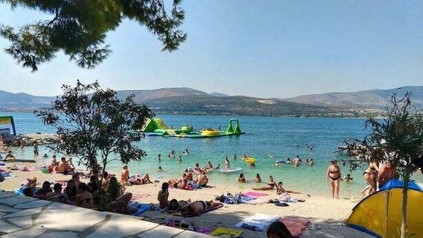 A beach with people sunbathing and swimming, a clear sky, and mountains in the background. - Mastrinka Bright Apartment With Free Parking and Modern Amenities (Trogir)