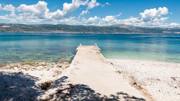 A concrete pier extending into a clear blue sea with a distant shoreline and mountains. - Seaside Getaway Holiday Home With Patio Slatine (Split)