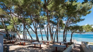 A beachside area with picnic tables and a building, overlooking a clear blue sea. - Seaside Getaway Holiday Home With Patio Slatine (Split)