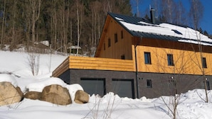 A cabin with a wooden exterior, a metal roof, and a garage. - Holiday Villa in Beautiful Location (Bedrichov)