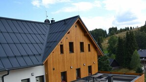 A modern building with a sloped roof, a wooden exterior, and a patio area with benches and a barbecue grill. - Holiday Villa in Beautiful Location (Bedrichov)