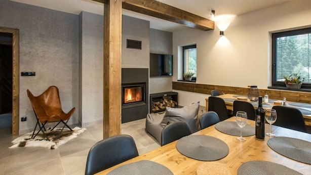 A modern dining area with a wooden table, grey placemats, and a fireplace. - Holiday Villa in Beautiful Location (Bedrichov)
