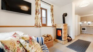 A cozy living room with a sofa, a fireplace, a TV mounted on the wall, and a kitchen area visible through an open door. - Beautiful Villa With Activities (Varvažov)