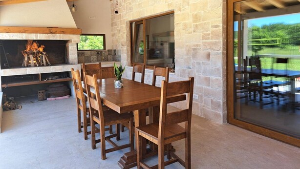 Zona pranzo con parete in pietra, soffitto in legno e ampia finestra vista giardino.
