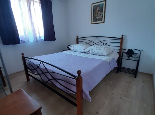 A bedroom with a metal bed frame, a wooden nightstand, a small table, and a window with curtains. - Tranquil Holiday Home With Pool, Garden, and Playground in a Peaceful Countryside Setting (Sinj)