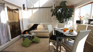 A modern living room with a sofa, a dining table with chairs, a coffee table, and a large plant.