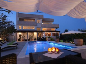 Una casa moderna de dos pisos con piscina, mobiliario exterior y grandes ventanales.