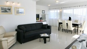 A modern living room with a black sofa, a beige armchair, and a dining area with a table and chairs.