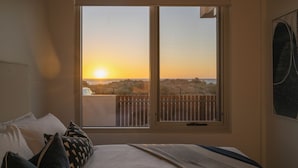 Ein Schlafzimmer mit großem Fenster mit Blick auf einen Strand bei Sonnenuntergang.