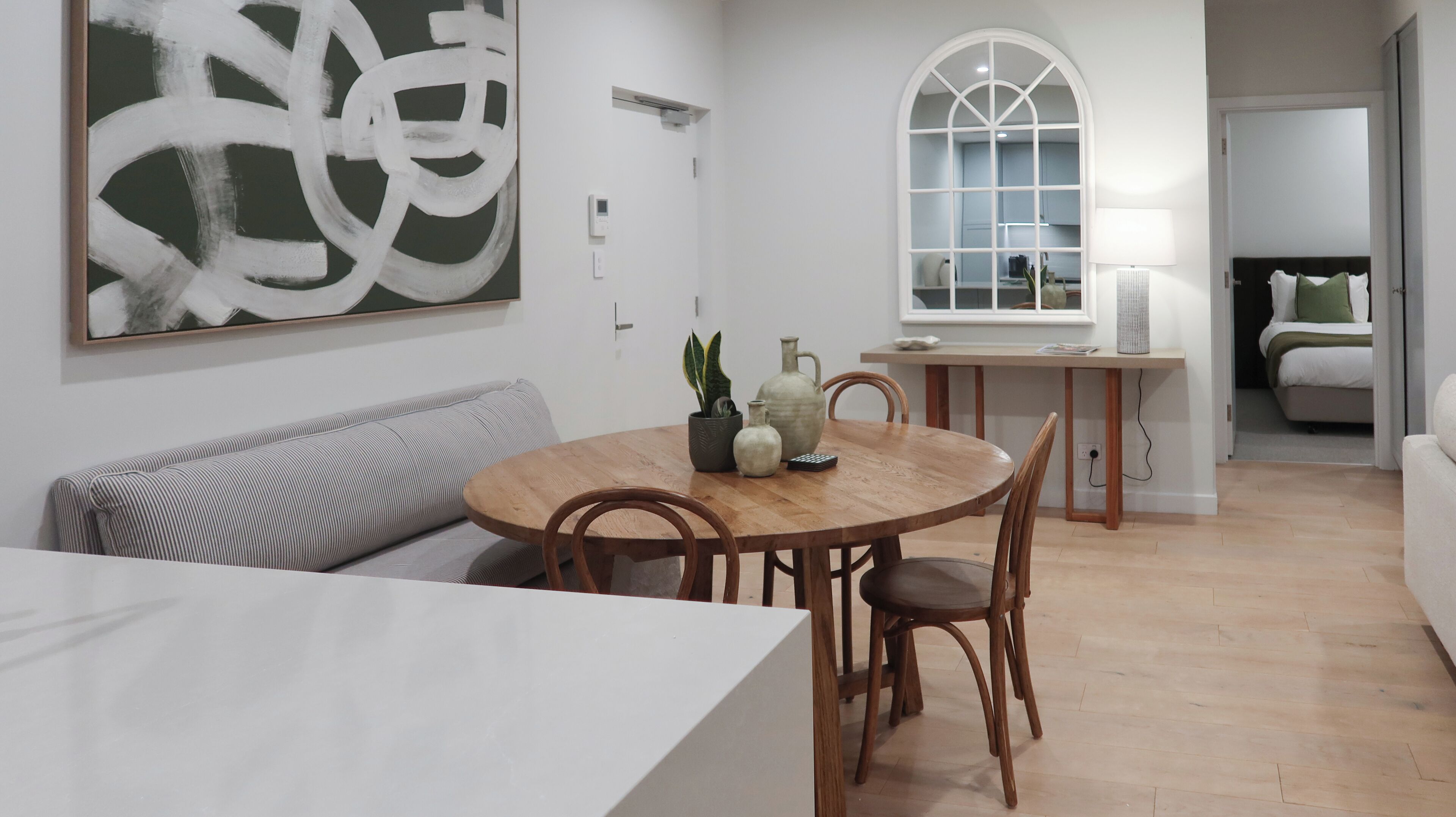 Un soggiorno moderno con zona pranzo, caratterizzato da un tavolo rotondo in legno, due sedie in legno, un divano a righe e un grande quadro astratto appeso al muro.