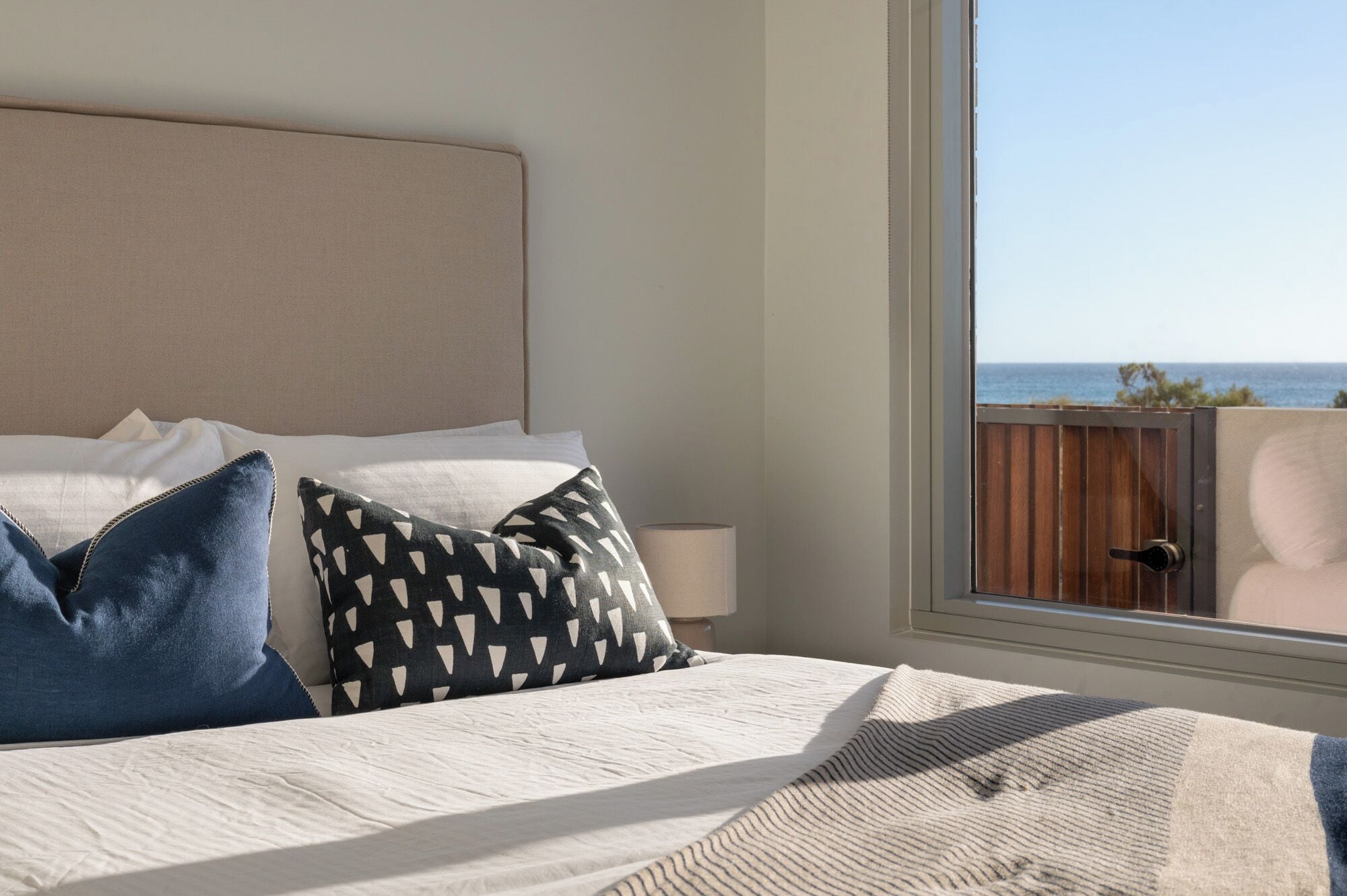 Una camera da letto con un letto grande, due cuscini, una lampada da comodino e vista sull'oceano attraverso una finestra.