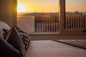 Sängyssä on kuviollisia tyynyjä, ja ikkunasta, jossa on puinen kaide, avautuu näkymä auringonlaskuun.