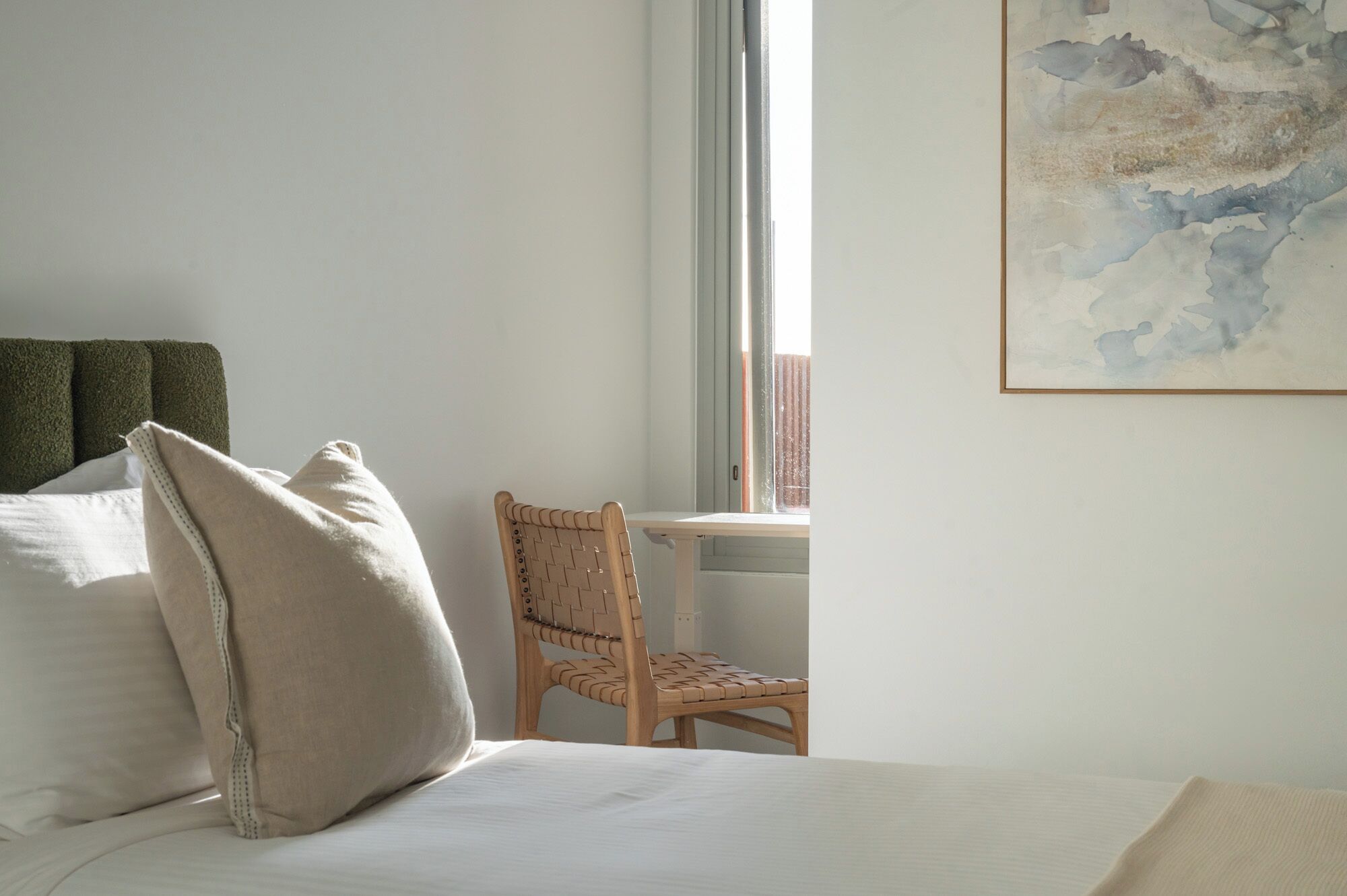 Quarto de hotel com uma cama, uma cadeira, uma janela e um quadro na parede.