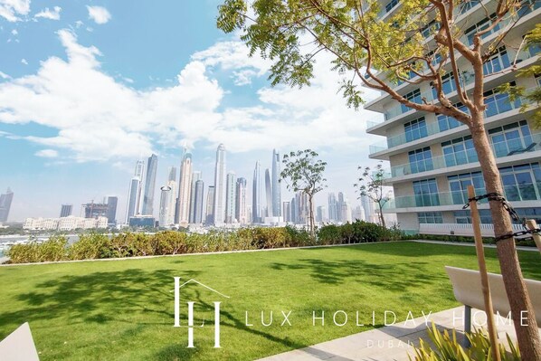 A luxury holiday home with a view of the Dubai skyline, a well-maintained lawn, and a modern building structure.
