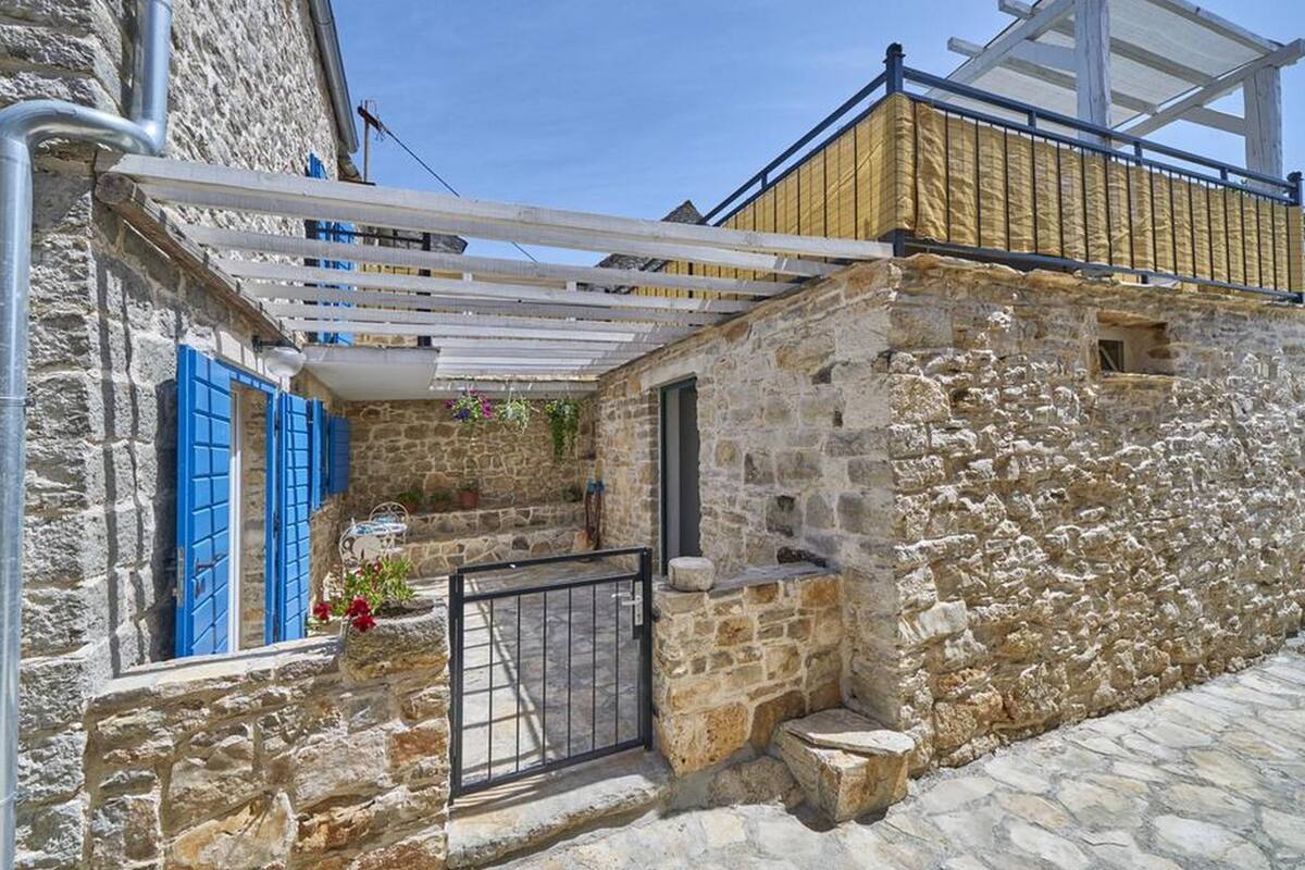 A stone building with a wooden balcony, a metal gate, and a small garden area with potted plants.