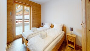 A bedroom with two beds, wooden walls, a sliding glass door to a balcony, and a bedside table with a lamp. - Apartment With Comfortable Arrangements (Veysonnaz)
