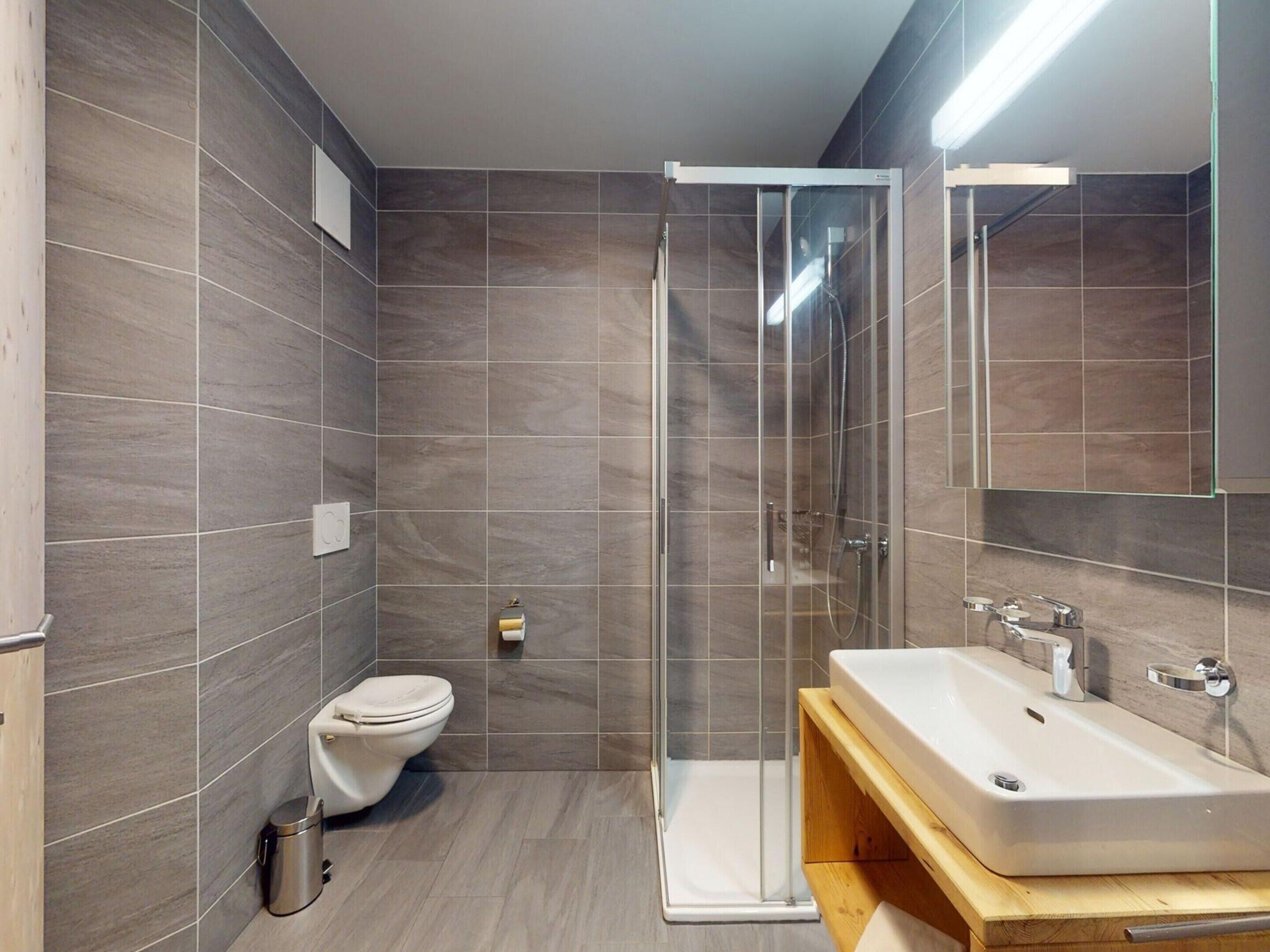 Ein modernes Badezimmer mit Duschkabine aus Glas, Toilette in Weiß und Holzwaschtisch.