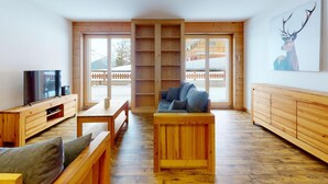 A modern living room with wooden furniture, a television, and a large window with a view of a snowy landscape. - Apartment With Comfortable Arrangements (Veysonnaz)
