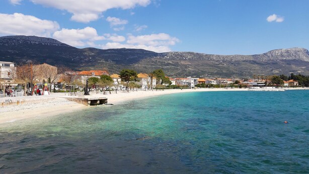 Eine Küstenstadt mit sandigem Strand, klarem türkisblauem Wasser und einer Bergkulisse.