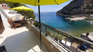 Un balcon avec un parasol jaune, une table et des chaises, et une vue sur une zone côtière avec des bateaux et des falaises.