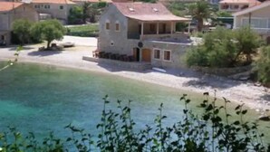 Un village côtier aux bâtiments en pierre, bordé d’une mer d’un bleu limpide et entouré d’une végétation luxuriante.