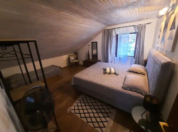 A bedroom with a sloped ceiling, a bed with pillows and a blanket, a bedside table, a lamp, and a window with curtains. - Apartment Katarina (Jelsa)