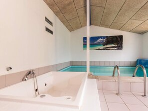 A spa room with a large bathtub, a smaller pool, and a wall-mounted picture of a beach scene. - 4 Star Holiday Home in Vaeggerlose (Vaeggerlose)